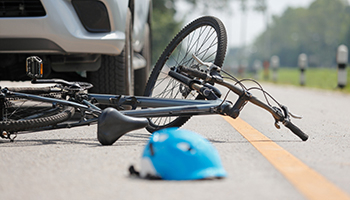 A bicycle lies on the roadside next to a car, indicating a recent bicycle accident